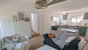 A modern living room with a sofa, a coffee table, and a TV. There is a kitchen area with a window and cabinets. - House with garden, walking distance to the beach (Pornichet)