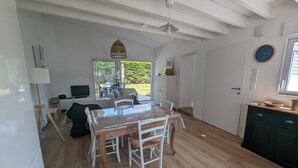 A spacious living area with a wooden dining table, white chairs, a sofa, and a television. There is a large window providing a view of the outdoors. - House with garden, walking distance to the beach (Pornichet)