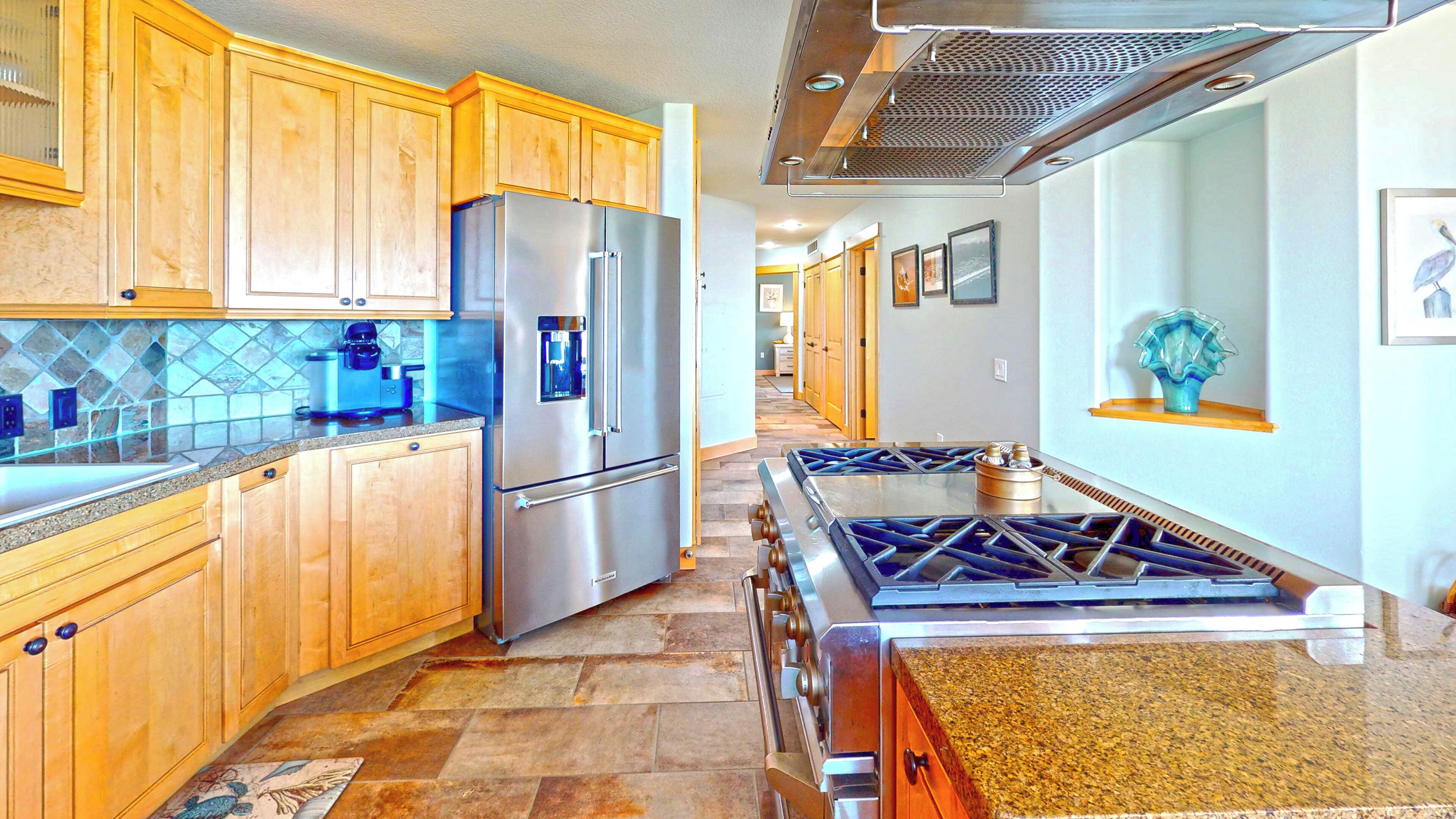 A kitchen with wooden cabinets, a stainless steel refrigerator, a gas stove, and a tiled backsplash.