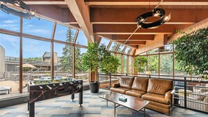 A spacious indoor area with a foosball table, leather sofa, and large windows offering a view of the outdoors. - Best Of Summit 2025 Winner for Best Lodging Hotel! Wonderful Breckenridge Locati (Breckenridge)