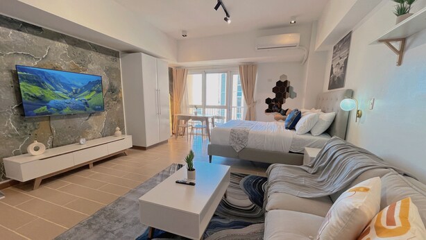 A modern living room with a flat-screen TV, a sofa, a coffee table, and a dining area with a table and chairs. - BGC 1BR, Steps to Venice Mall, 300Mbps Fiber 16K (Taguig)