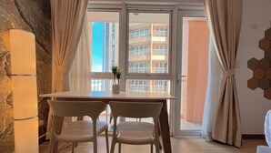 A modern room with a dining table and chairs, a potted plant, and a view of a building through a glass door. - BGC 1BR, Steps to Venice Mall, 300Mbps Fiber 16K (Taguig)