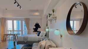 A modern hotel room with a bed, a sofa, a desk, and a large mirror. - BGC 1BR, Steps to Venice Mall, 300Mbps Fiber 16K (Taguig)