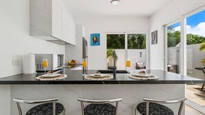 Une cuisine moderne avec un plan de travail noir, trois tabourets de bar, une grande fenêtre et un tableau accroché au mur.