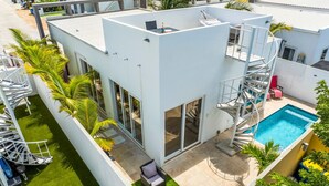 Une maison moderne à deux étages dotée d’une piscine sur le toit, d’un escalier en colimaçon et d’un petit patio aménagé avec du mobilier d’extérieur.