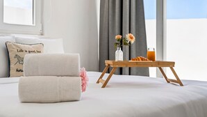 Un lit bien fait, avec une serviette pliée, un plateau contenant un croissant et une boisson, et un vase rempli de fleurs.