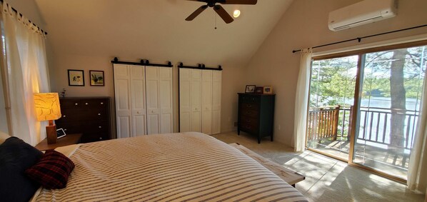 A bedroom with a bed, a nightstand, a lamp, a dresser, a wardrobe, and a balcony with a view of trees.