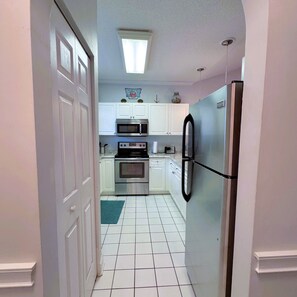 A narrow kitchen with white cabinets, a stainless steel refrigerator, and a microwave.