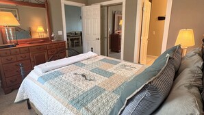 A bedroom with a large bed, a dresser, a mirror, and a door leading to another room. - Pet Friendly 2BR Condo, Spacious w/ Vaulted Ceilings! (Little River)