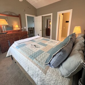 A bedroom with a large bed, a dresser, a mirror, and a door leading to another room. - Pet Friendly 2BR Condo, Spacious w/ Vaulted Ceilings! (Little River)