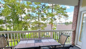 A covered patio with a table and chairs, a white railing, and a view of trees and houses. - Pet Friendly 2BR Condo, Spacious w/ Vaulted Ceilings! (Little River)