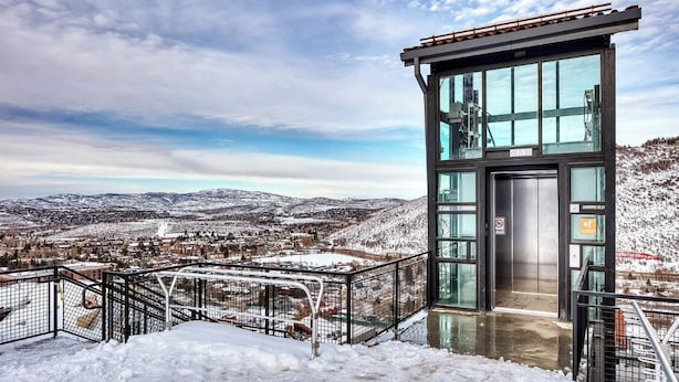 A modern observation tower with a glass elevator, surrounded by snow-covered hills and a cityscape in the background. - Modern Old Town Home by InvitedHome | Ski-In/Out, Walk to Town, Hot Tub (Park City)