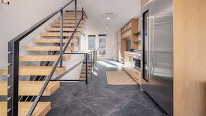 A modern kitchen with a stainless steel refrigerator, wooden cabinets, and a staircase with wooden steps and metal railings. - Modern Old Town Home by InvitedHome | Ski-In/Out, Walk to Town, Hot Tub (Park City)