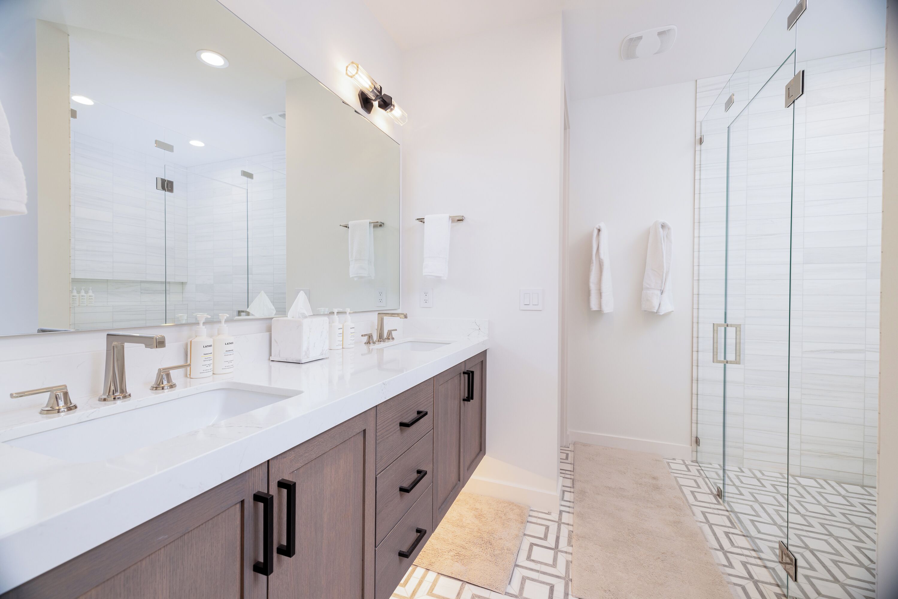 A modern bathroom with a large mirror, two sinks, and a glass shower enclosure.