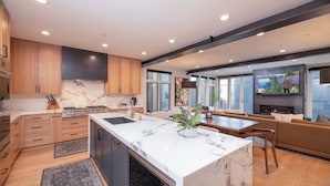A modern kitchen with marble countertops, wooden cabinets, and a central island. - Modern Old Town Home by InvitedHome | Ski-In/Out, Walk to Town, Hot Tub (Park City)