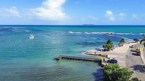 A coastal area with a pier extending into the sea, a sandy beach, and a clear blue sky.