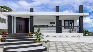 A modern two-story house with a white facade, dark columns, and a balcony with outdoor seating.