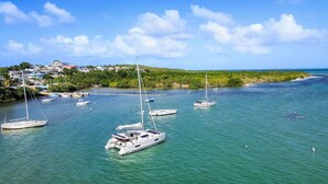 A marina with multiple sailboats docked, surrounded by lush greenery and a clear blue sky.