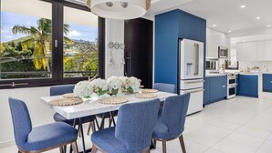A modern kitchen with blue cabinets, a white refrigerator, and a dining area with blue chairs and a white table.