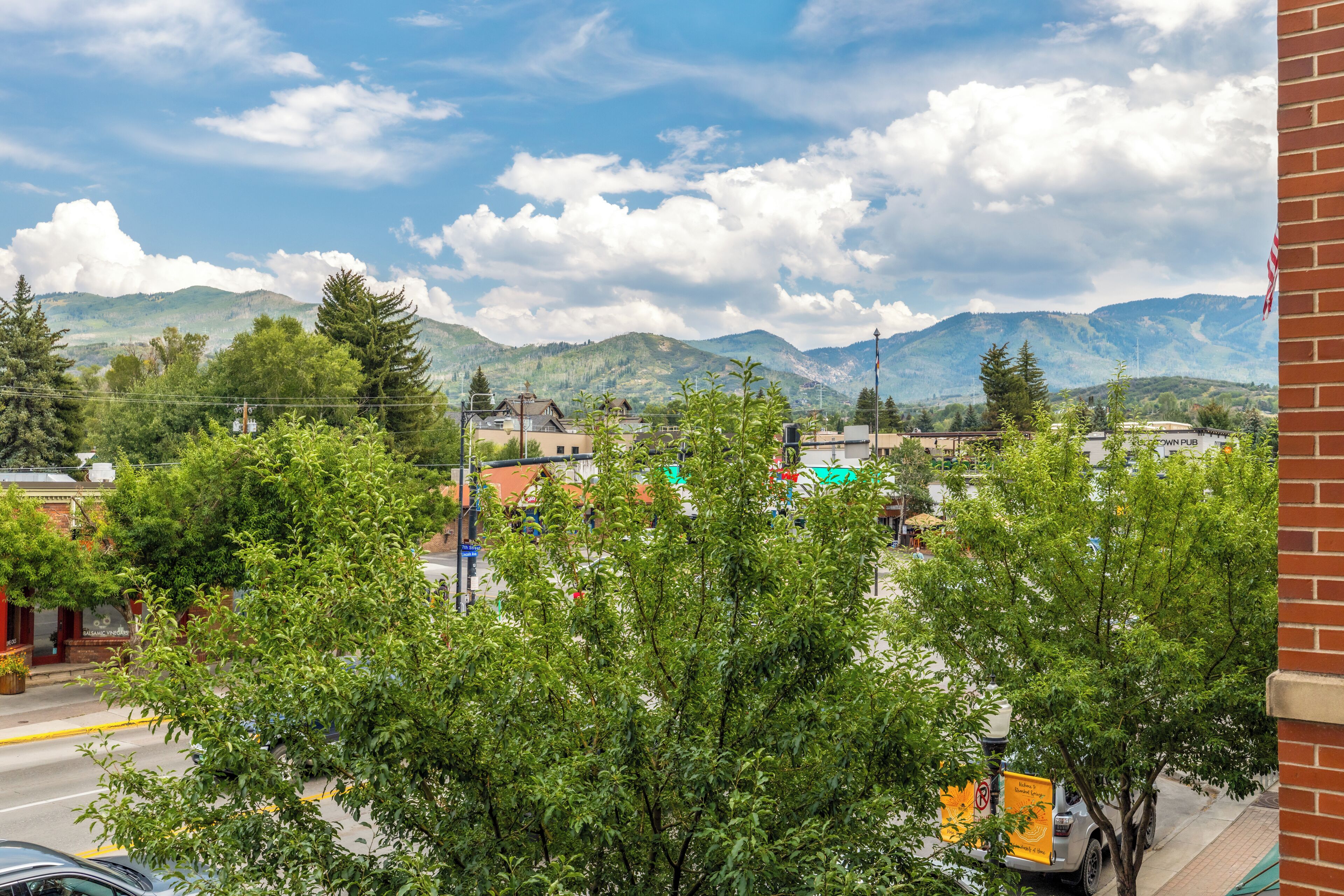 Une vue d’une ville avec des montagnes en arrière-plan, une rue avec des voitures et des arbres au premier plan.