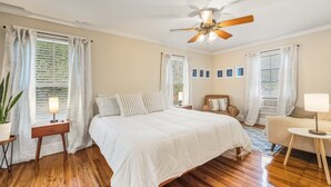 Ein Schlafzimmer mit einem großen Bett, einem Deckenventilator, Holzboden und einem kleinen Tisch mit Lampe.
