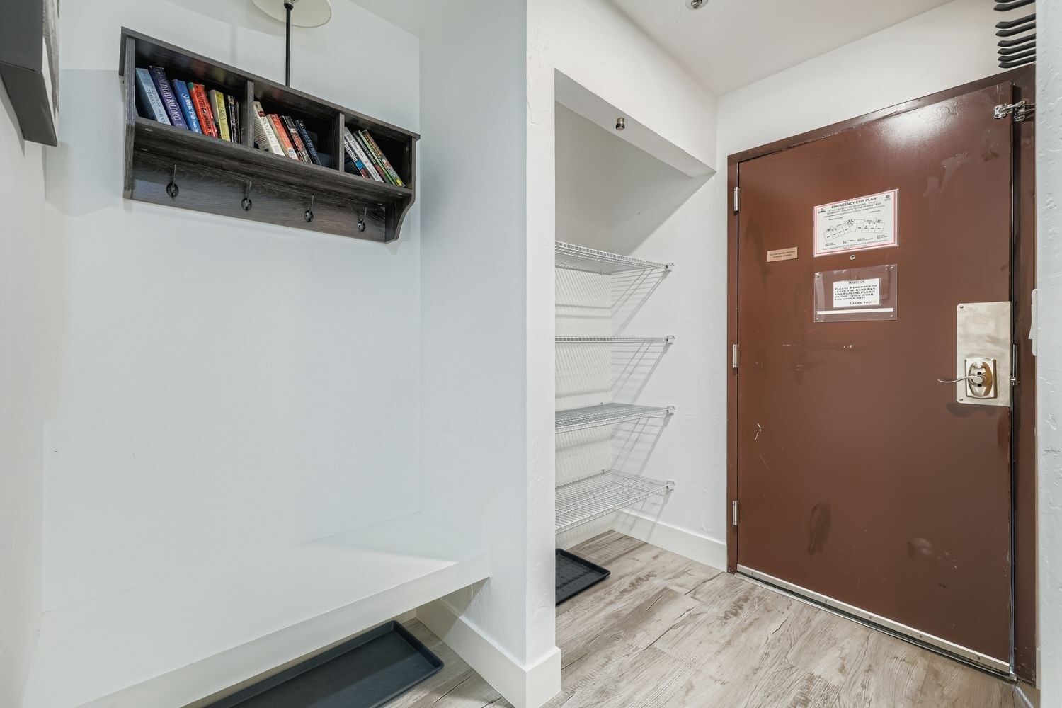 A room with a wooden bookshelf, a brown door with emergency exit plan, and a metal shelf unit.