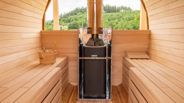 Een sauna met houten banken, een stenen wasbak en een Harvia sauna-oven.