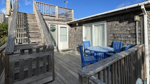 A wooden deck with a table and chairs, a door, and a staircase leading to a balcony. - Chasing Sunsets 4 Bedroom Cottage (Hatteras)