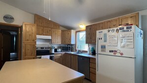 A kitchen with wooden cabinets, a refrigerator, a microwave, and a dishwasher. - Chasing Sunsets 4 Bedroom Cottage (Hatteras)