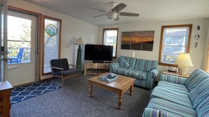 A living room with a sofa, armchair, coffee table, TV, and ceiling fan. - Chasing Sunsets 4 Bedroom Cottage (Hatteras)