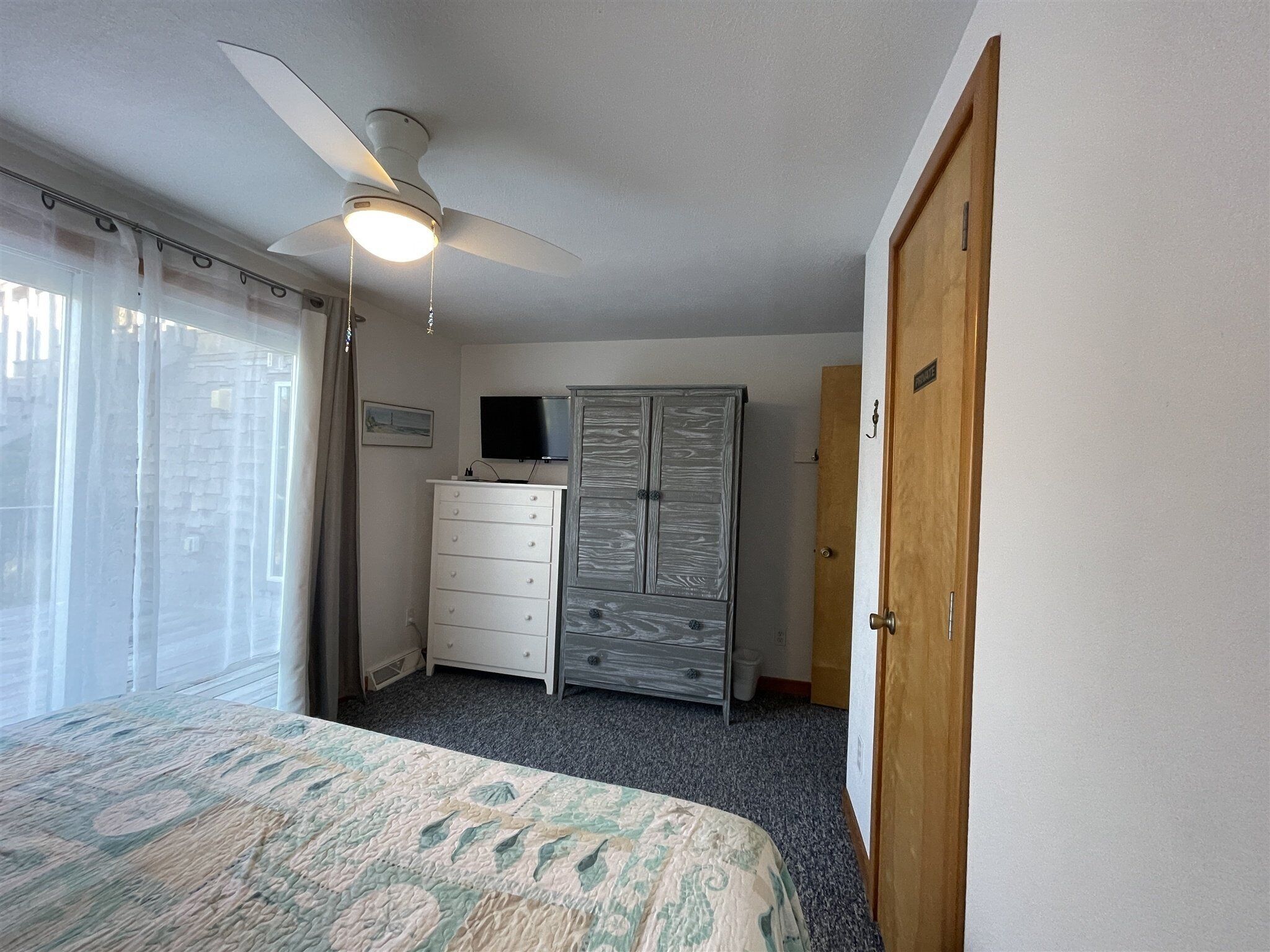 A bedroom with a bed, a dresser, a wardrobe, a ceiling fan, and a television.