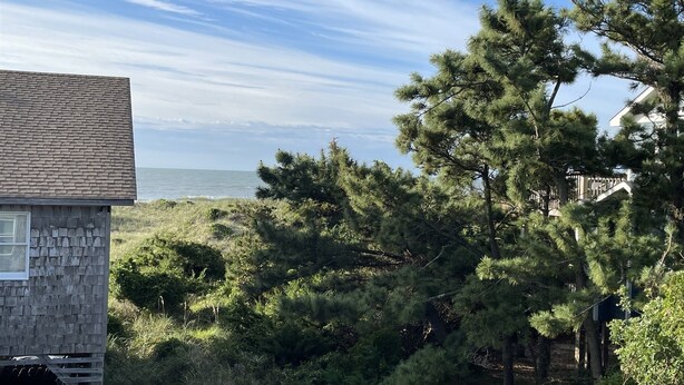 A coastal view with a stone building, dense pine trees, and a clear sky. - Chasing Sunsets 4 Bedroom Cottage (Hatteras)