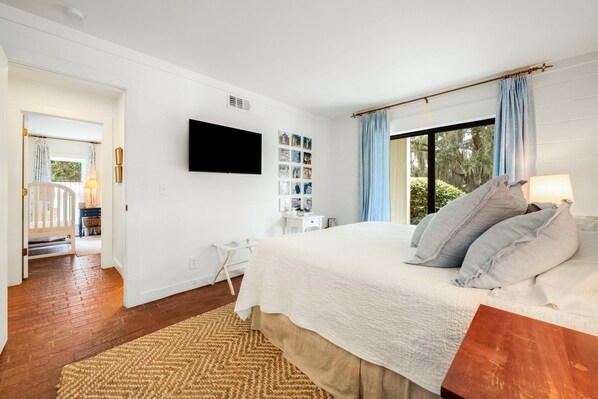 Un dormitorio con una cama grande, un televisor de pantalla plana, una mesita de noche pequeña y una ventana con cortinas.
