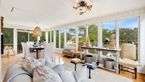 A spacious room with large windows, a white sofa, a dining table, and a chandelier. - Sunny Pointe 4 Bedroom Home (Georgetown)