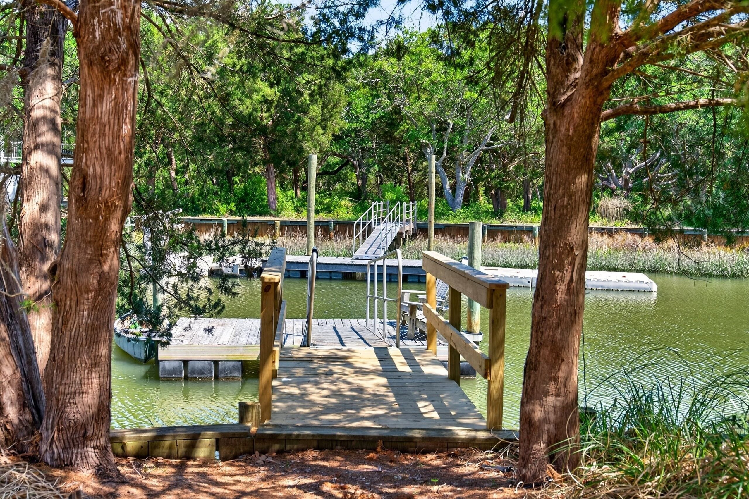 A wooden dock leading to a small island with a railing, surrounded by trees and a body of water.