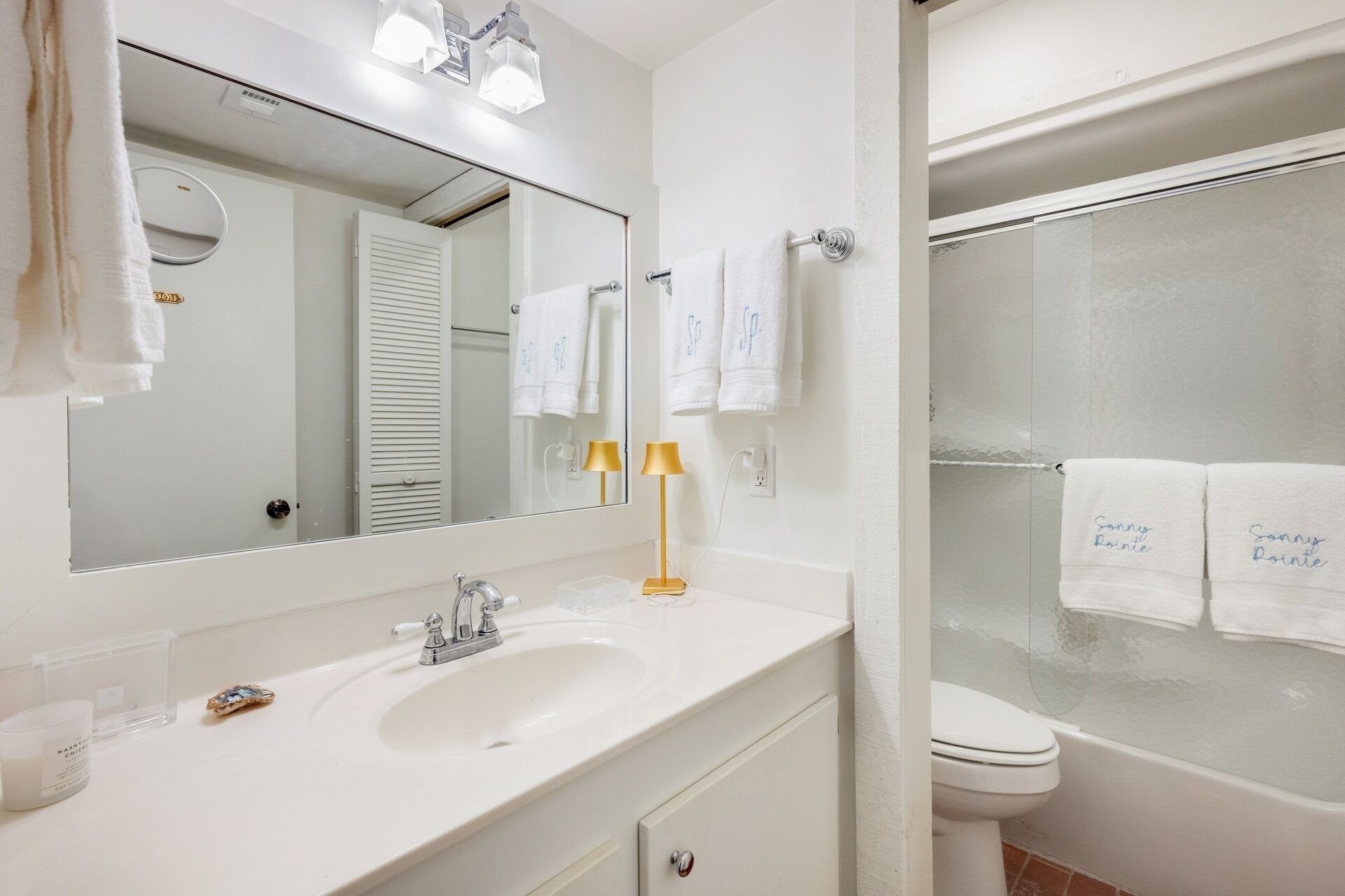 A bathroom with a sink, mirror, two towels, a toilet, and a shower.