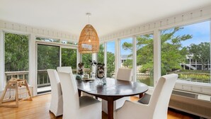 A dining area with a round table, white chairs, a wicker pendant light, and a view of a lake through large windows. - Sunny Pointe 4 Bedroom Home (Georgetown)