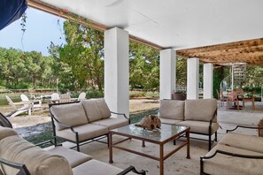 An outdoor seating area with sofas and tables, surrounded by greenery and a pool. - Sunny Pointe 4 Bedroom Home (Georgetown)
