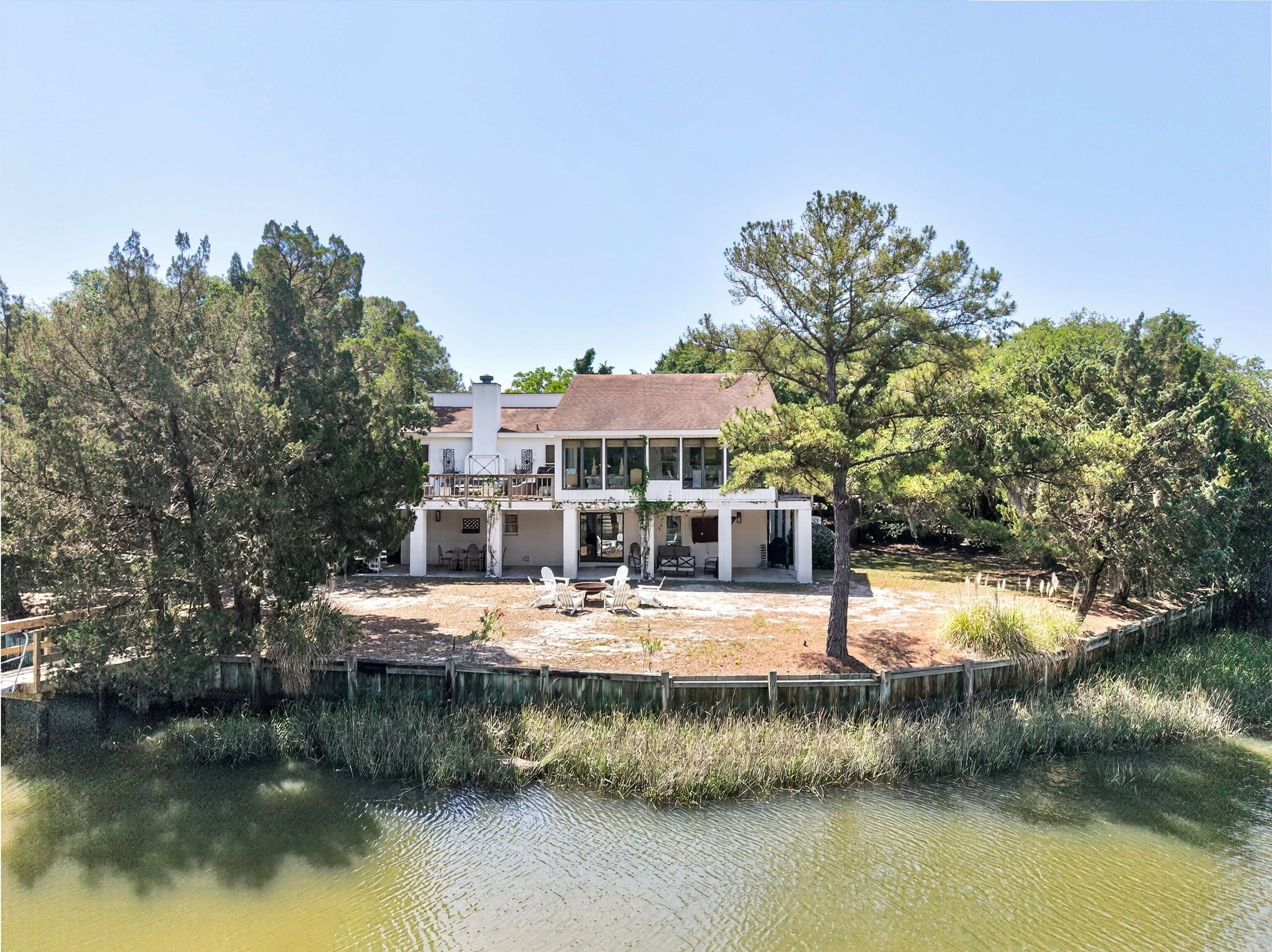 A two-story house with a large deck, surrounded by trees and a pond.