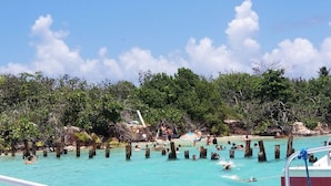 Una playa con aguas turquesas cristalinas, gente nadando y un barco amarrado cerca.