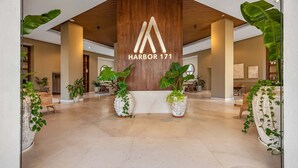 Un vestíbulo amplio con techo de madera, grandes plantas en macetas y un cartel llamativo que dice 'Harbor 171'.