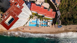 Vista aérea de un hotel frente al mar, con varias piscinas, una playa y un río.