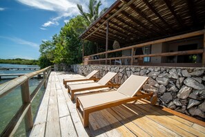 Une terrasse en bois avec des chaises longues, un mur en pierre et une vue sur l’eau.