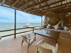 Un salon de plage avec vue sur l’océan, un hamac et une table à manger avec des chaises.