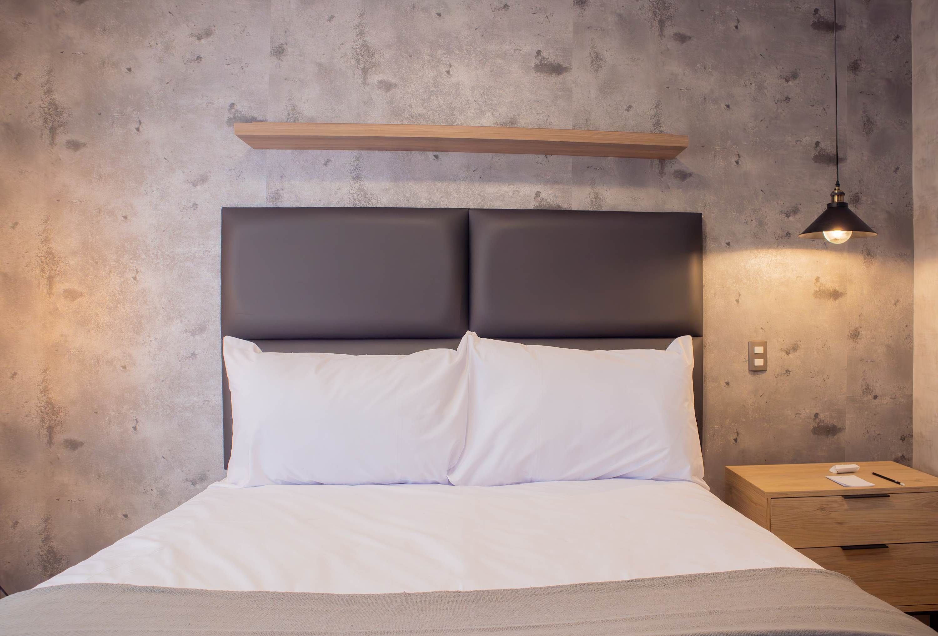 A bed with a headboard, white bedding, a wooden nightstand, and a pendant light.