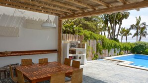An outdoor patio with a wooden table and chairs, a pool, and a bamboo pergola. - w Modern 5BR With Private Pool in Paracas (Paracas)