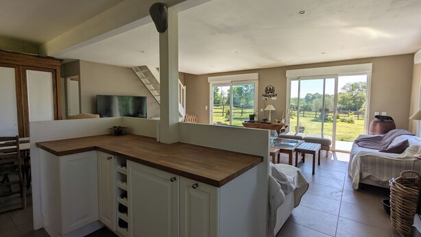 A spacious living area with a kitchen, a dining table, and a large sliding glass door leading to a garden.