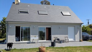 A two-story house with a grey roof, large sliding glass doors, and a patio area with outdoor furniture.