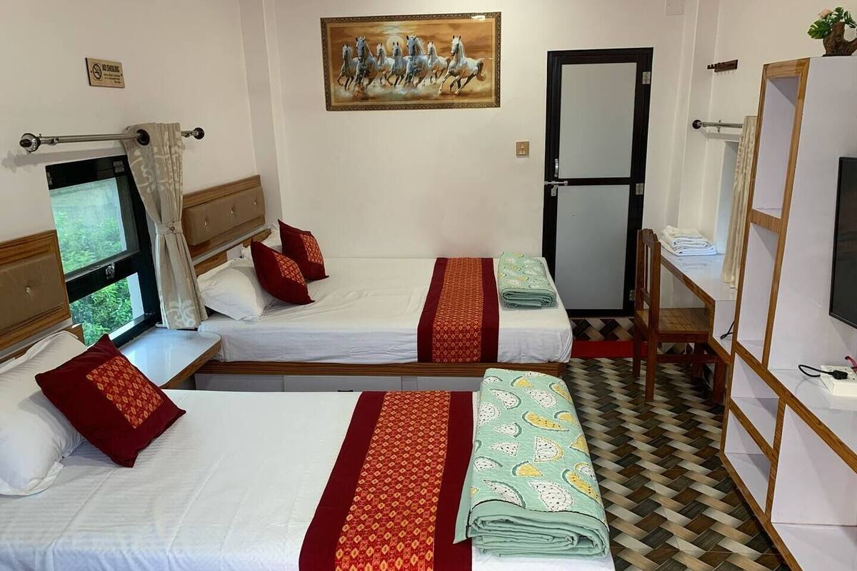 Habitación de hotel con dos camas, un televisor, una puerta y un cuadro en la pared.