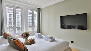 A hotel room with a large bed, a flat-screen TV mounted on the wall, and a balcony with a view of buildings. - Modern Apartment - 1br/4p - Canal St-martin (Paris)